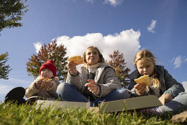 Schwestern essen Pizza im Park sitzend - SSGF00076