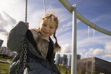 Carefree girl sitting on swing in playground - SSGF00082