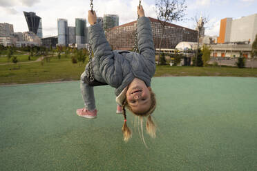 Girl bending backwards while sitting on swing in playground - SSGF00084