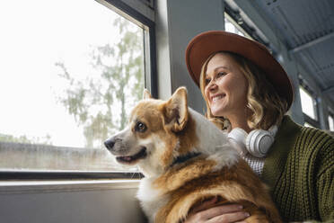 Lächelnde Frau, die mit ihrem Hund durch das Fenster schaut, während sie im Zug reist - VPIF05112