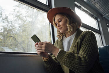 Mittlere erwachsene Frau, die ein Smartphone benutzt, während sie im Zug sitzt - VPIF05113