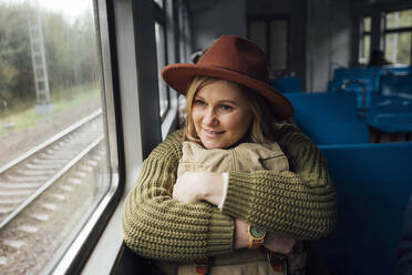 Frau hält Rucksack und schaut durch ein Fenster im Zug - VPIF05117