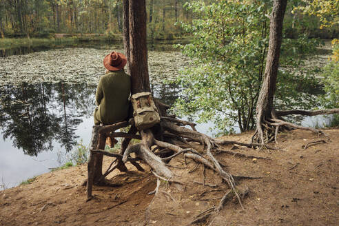 Frau schaut auf einen See, während sie in der Nähe eines Baumes im Wald sitzt - VPIF05123