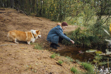 Junge taucht einen Stock ins Wasser, während er in der Nähe eines Sees im Wald hockt - VPIF05127