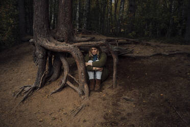 Einsame Frau, die ihre Knie umarmt und unter einem Baum im Wald sitzt - VPIF05129