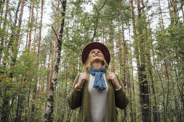 Frau mit Hut, die im Wald stehend nach oben schaut - VPIF05140