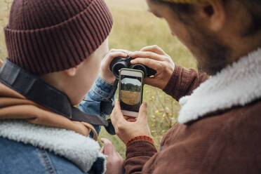 Vater und Sohn halten ein Fernglas vor einem Smartphone - VPIF05142