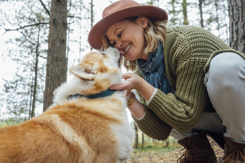 Hund leckt das Gesicht einer im Wald kauernden Frau - VPIF05147