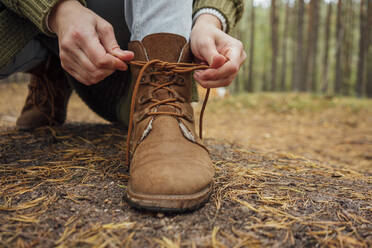 Frau bindet Schnürsenkel eines Stiefels im Wald - VPIF05148