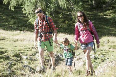 Glückliche Eltern halten die Hände ihres Sohnes beim Wandern auf einer Bergwiese im Urlaub - HHF05814