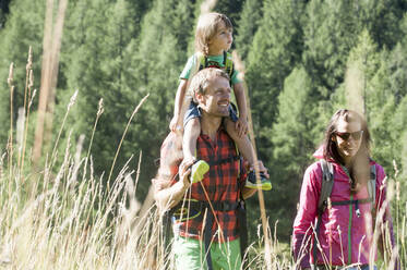 Smiling father carrying son on shoulders while hiking with woman during sunny day - HHF05818