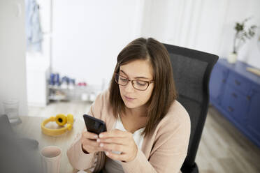 Female freelancer using smart phone while working at home - ZEDF04275
