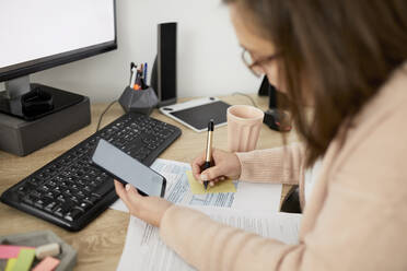 Geschäftsfrau hält Smartphone und schreibt am Schreibtisch sitzend - ZEDF04277