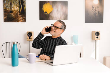 Smiling man talking on mobile phone in home office - GPF00097