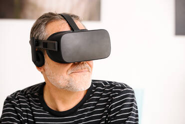 Mature man with hair stubble wearing virtual reality simulator at home - GPF00105