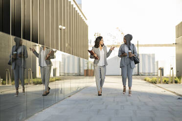 Female professionals talking while walking on footpath - JCCMF04286