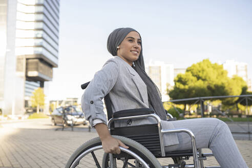 Lächelnde behinderte Frau im Rollstuhl sitzend auf dem Gehweg - JCCMF04307