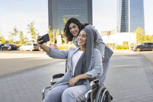 Lächelnde behinderte Geschäftsfrau macht Selfie mit Kollegin auf Gehweg - JCCMF04311