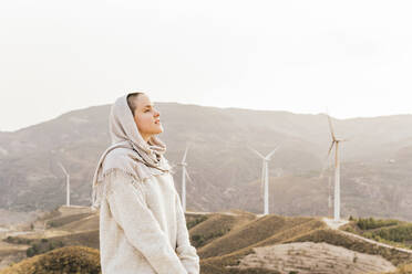 Nachdenkliche Frau mit Kopftuch vor einem Windpark - MGRF00548