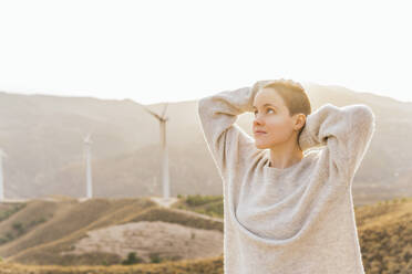 Rasierte Frau mit Hand hinter dem Kopf vor einem Windpark - MGRF00562