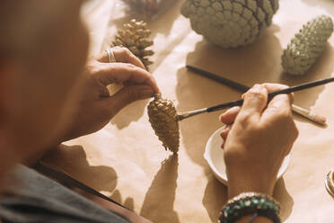 Female craftswoman painting pine cone on workbench - GPF00122