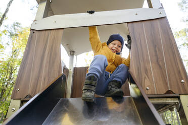 Happy boy playing on slide at park - EYAF01788