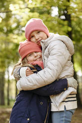 Girls wearing knit hat hugging each other at park - EYAF01791
