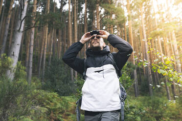 Männlicher Tourist schaut durch ein Fernglas im Wald - JCCMF04325