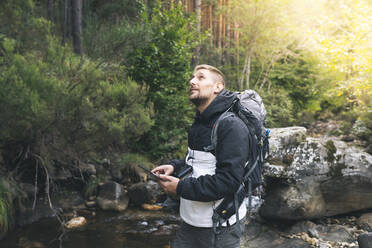 Männlicher Tourist mit digitalem Tablet, der im Wald nach oben schaut - JCCMF04330