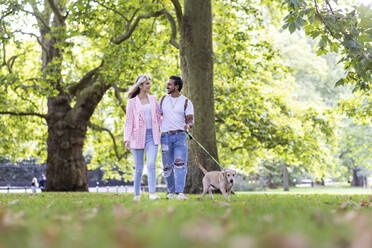 Lächelndes junges Paar, das sich beim Spaziergang mit Hund im Park ansieht - WPEF05350