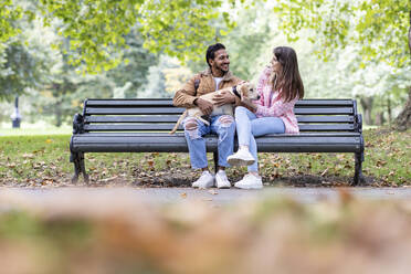 Glückliches junges Paar mit Hund sitzt auf einer Bank in einem öffentlichen Park - WPEF05360