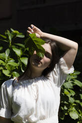 Teenager-Mädchen hält grünes Blatt vor geschlossenen Augen an einem sonnigen Tag - MRAF00644