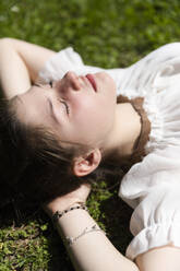 Mädchen mit geschlossenen Augen im Garten liegend an einem sonnigen Tag - MRAF00646