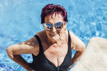 Senior woman wearing sunglasses while making a face in pool - EGHF00190