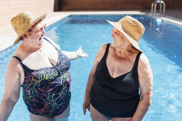 Senior women laughing in pool during sunny day - EGHF00192