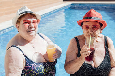 Ältere weibliche Freunde, die im Sommer im Schwimmbad Saft trinken - EGHF00195