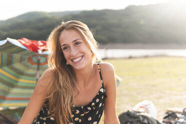 Beautiful young woman smiling at lakeshore during sunny day - JAQF00852