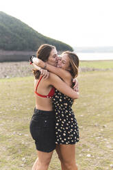 Happy female friends hugging each other at lakeshore - JAQF00854