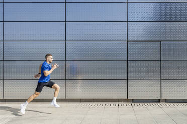 Young male athlete running by silver wall - IFRF01107