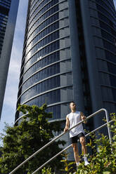 Junger männlicher Sportler, der an einem sonnigen Tag am Geländer steht - IFRF01127