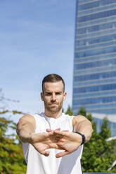 Sportsman with hands clasped stretching on sunny day - IFRF01131