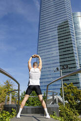 Young male athlete with arms raised exercising in city - IFRF01134