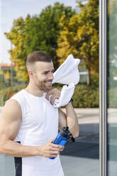 Sportsman holding water bottle and towel by glass wall - IFRF01147