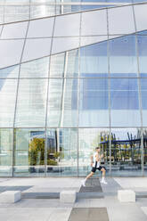 Junger männlicher Sportler, der auf dem Fußweg neben einem Glasgebäude läuft - IFRF01150