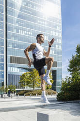 Sportler, der an einem sonnigen Tag vor einem Gebäude trainiert - IFRF01154