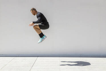 Male athlete jumping by wall during sunny day - IFRF01183