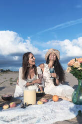 Female friends with drinks enjoying picnic on beach - RFTF00115