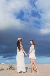 Smiling lesbian couple holding hands on beach - RFTF00132