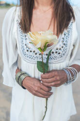 Mature woman holding flower at beach - RFTF00135