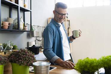 Smiling man holding coffee cup while standing in kitchen - GIOF13890
